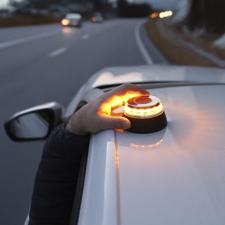 Mano colocando un dispositivo de alerta en el techo de un coche en la carretera.