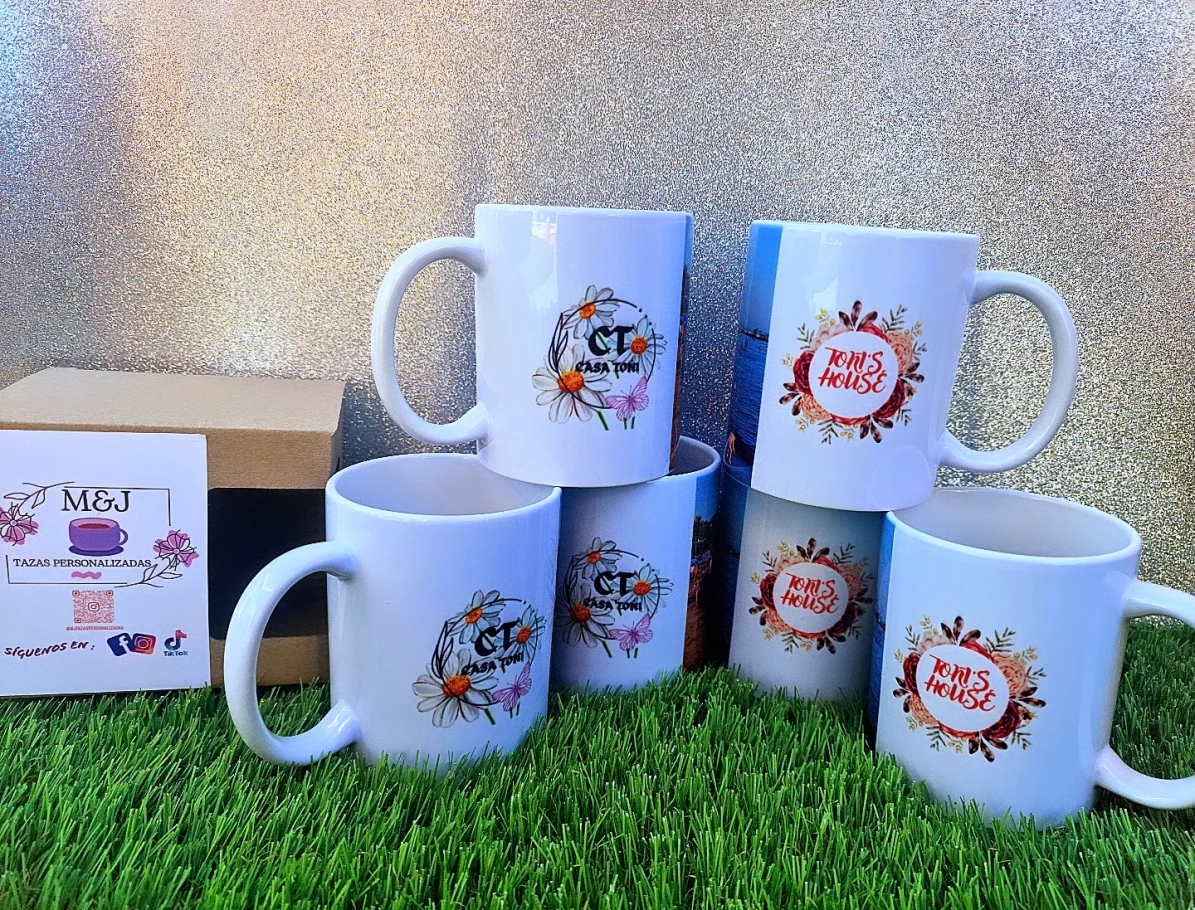 Cinco tazas blancas decoradas, apiladas sobre un fondo de césped artificial.